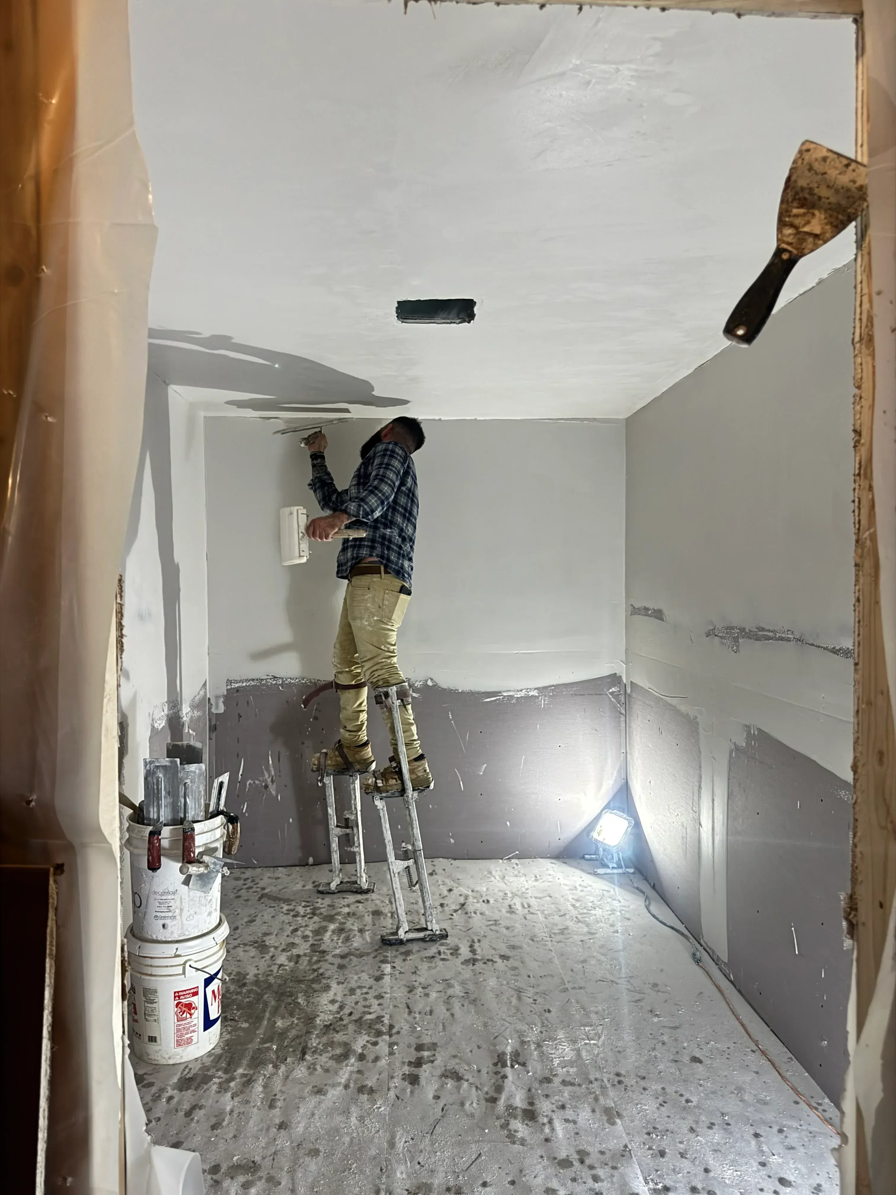 Worker applying drywall joint compound to taped seams on interior walls and ceiling