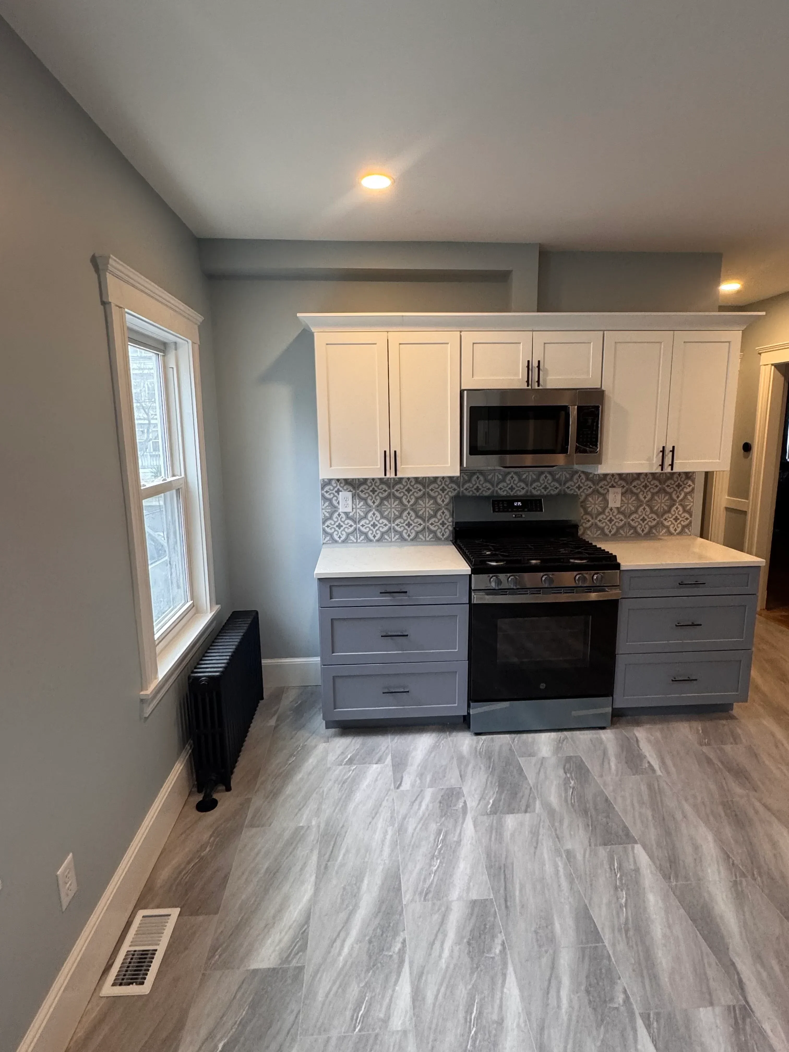 Custom kitchen with cream and gray cabinetry, black appliances, geometric backsplash tile, and wood-look vinyl flooring