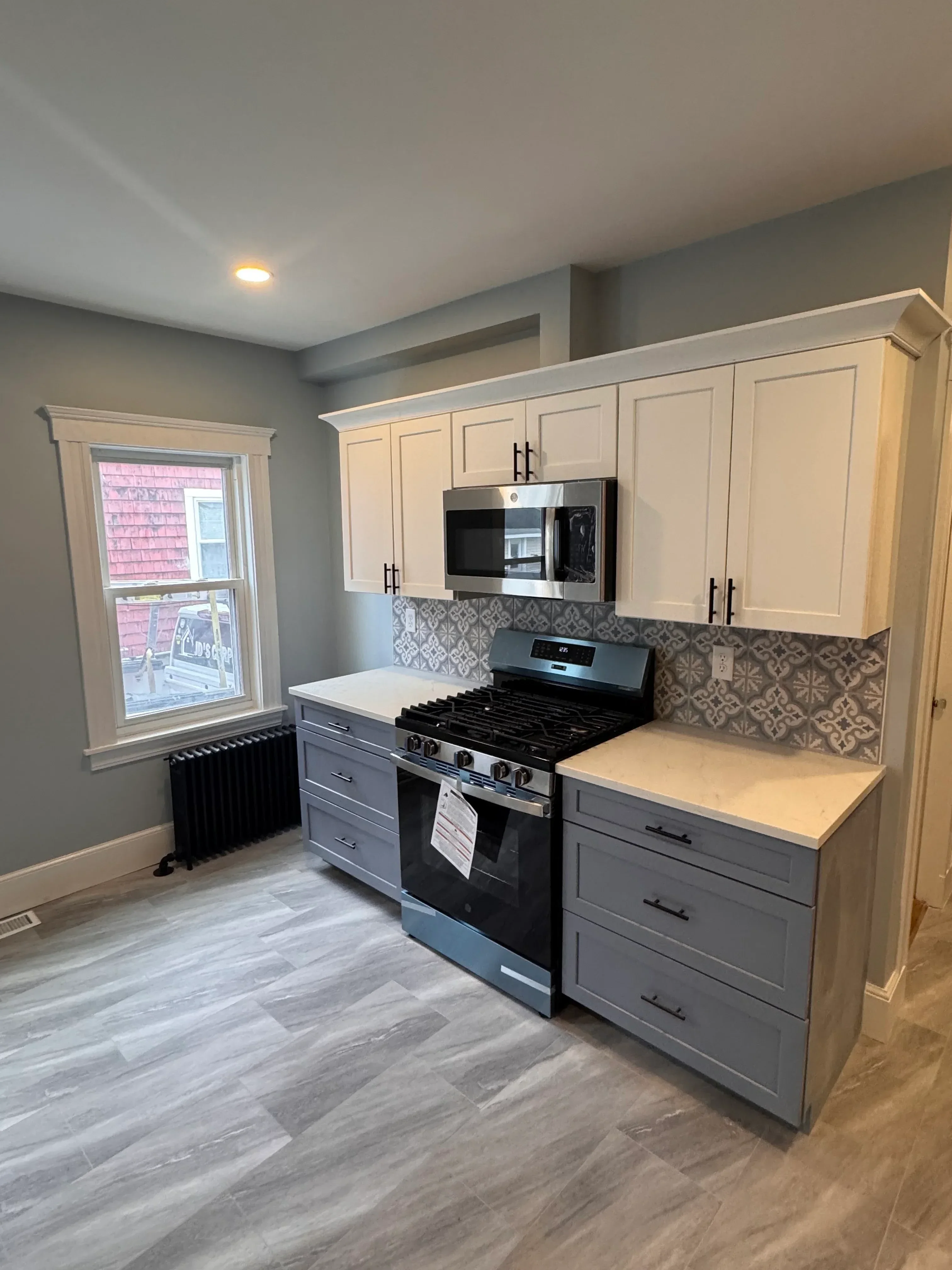 Kitchen with cream and blue painted cabinets, black countertops, gray vinyl plank flooring, and tile backsplash
