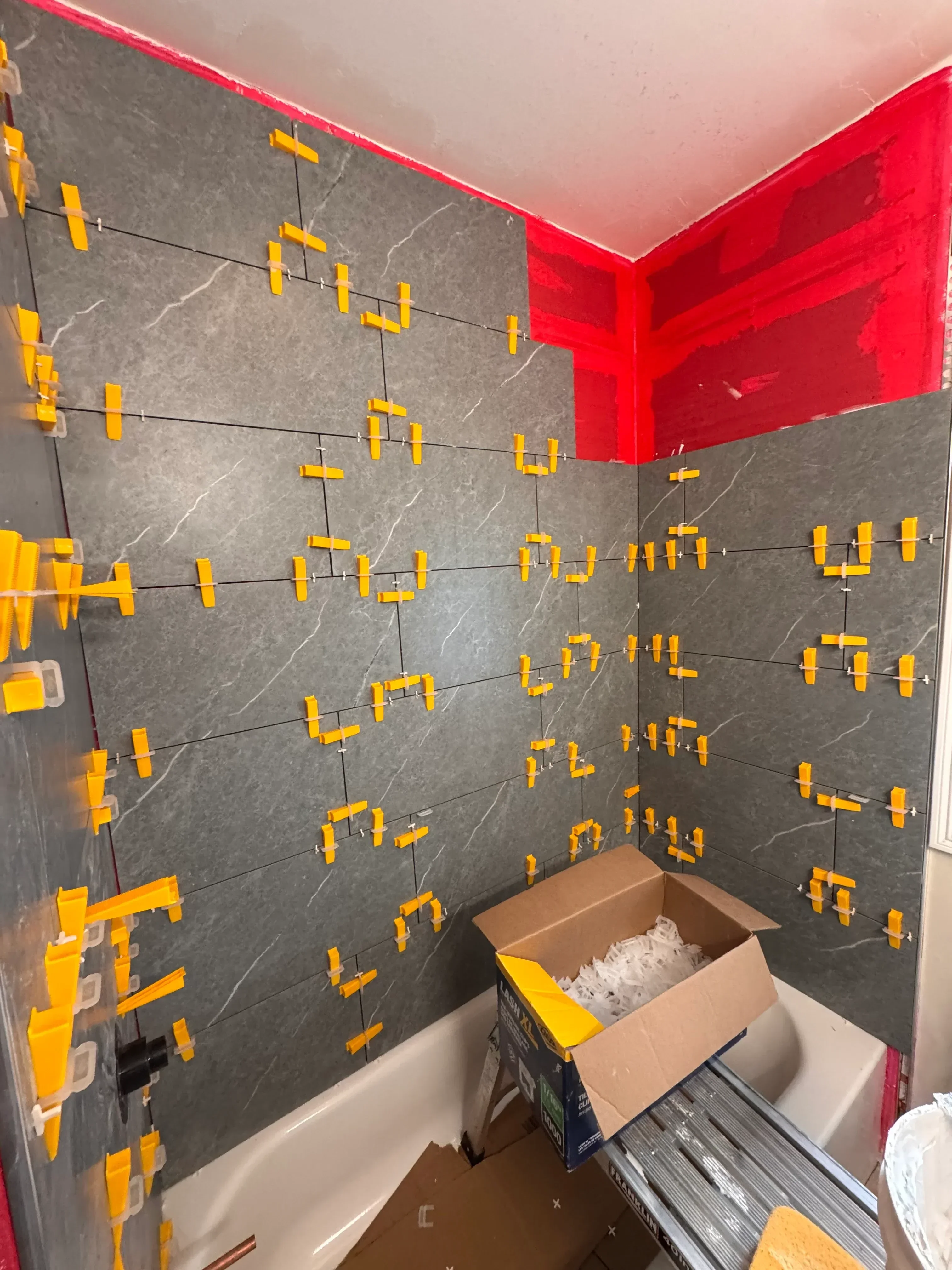 Dark gray porcelain tile floor with yellow spacers maintaining uniform grout lines during installation