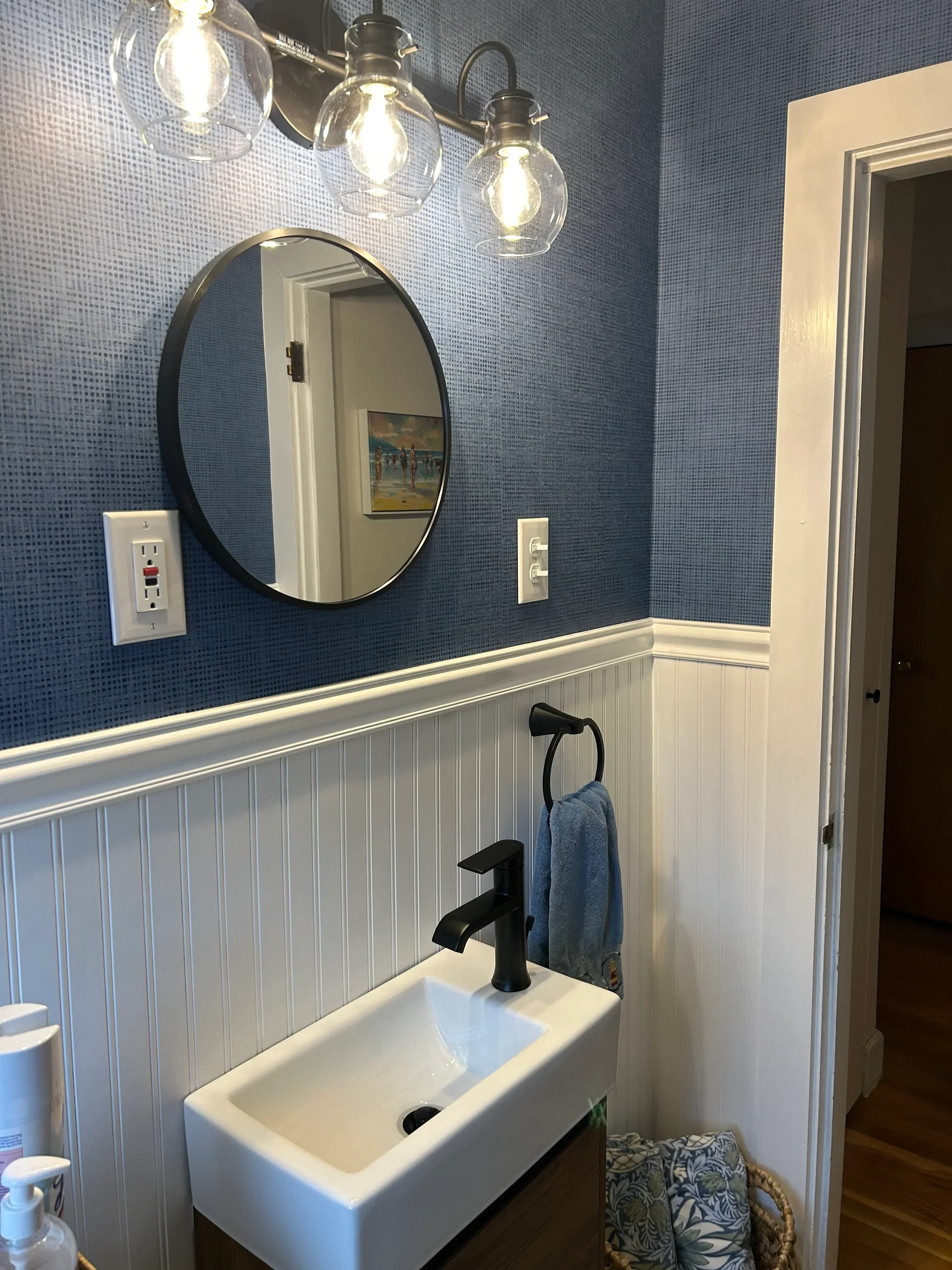Installed bathroom vanity with white cabinet, round mirror, and triple-bulb lighting fixture