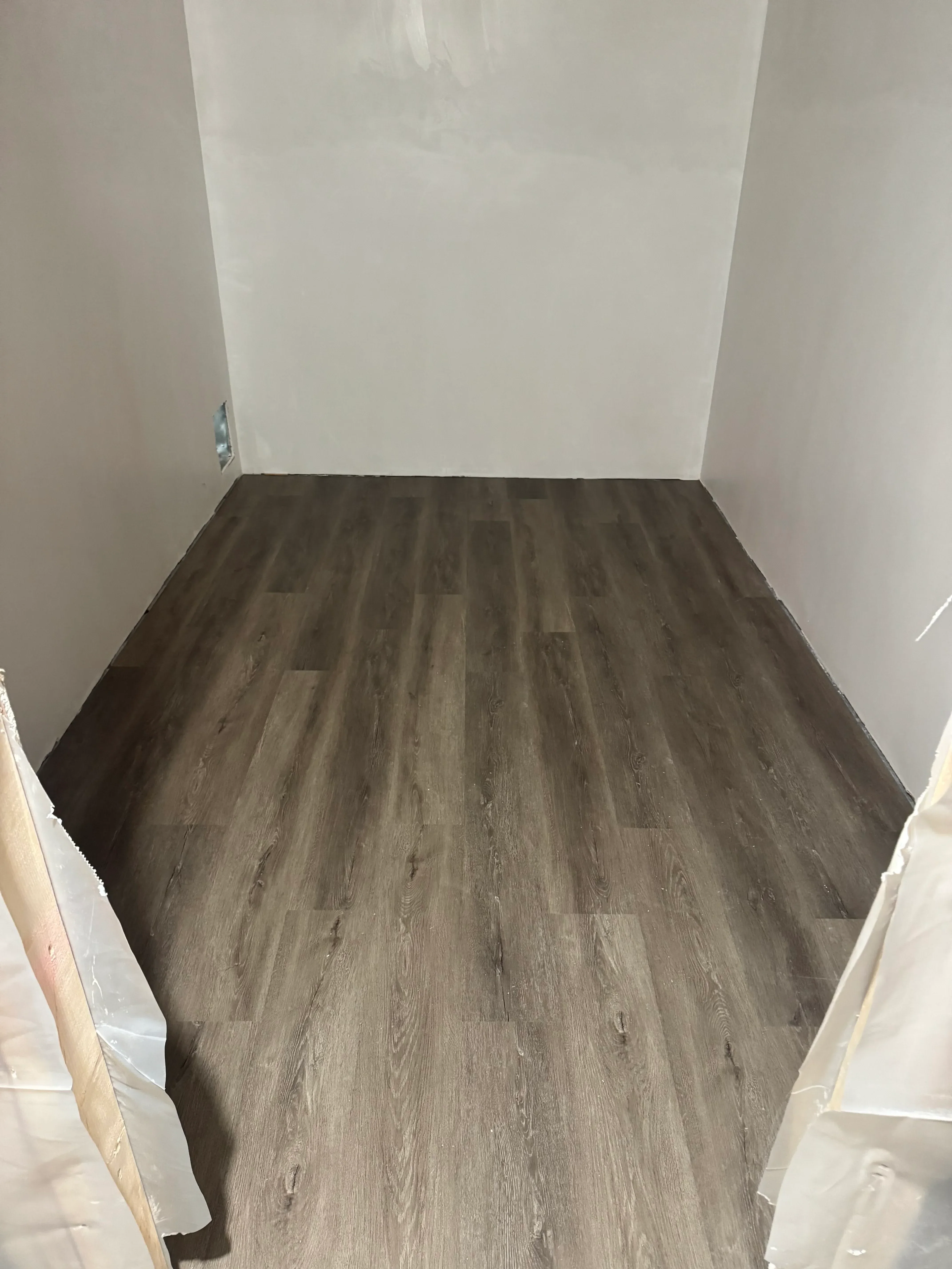 Dark wood-grain luxury vinyl plank flooring installed in staggered pattern with white drywall walls