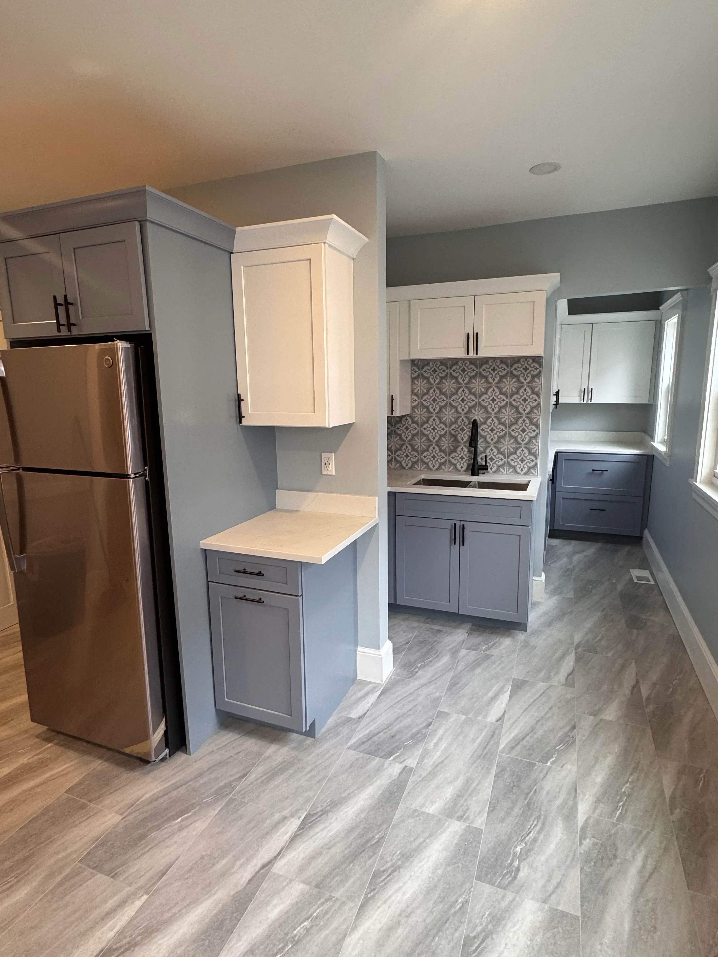 Installed kitchen cabinets with cream and gray painted finishes, shaker doors, and gray tile backsplash