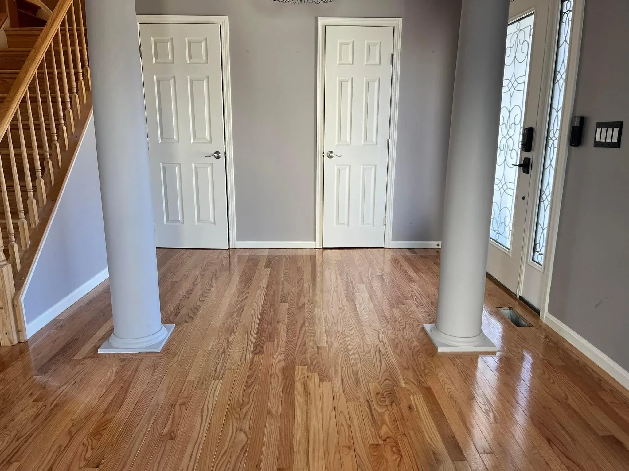 Hardwood oak flooring installation in foyer with white six-panel doors and support columns with custom bases