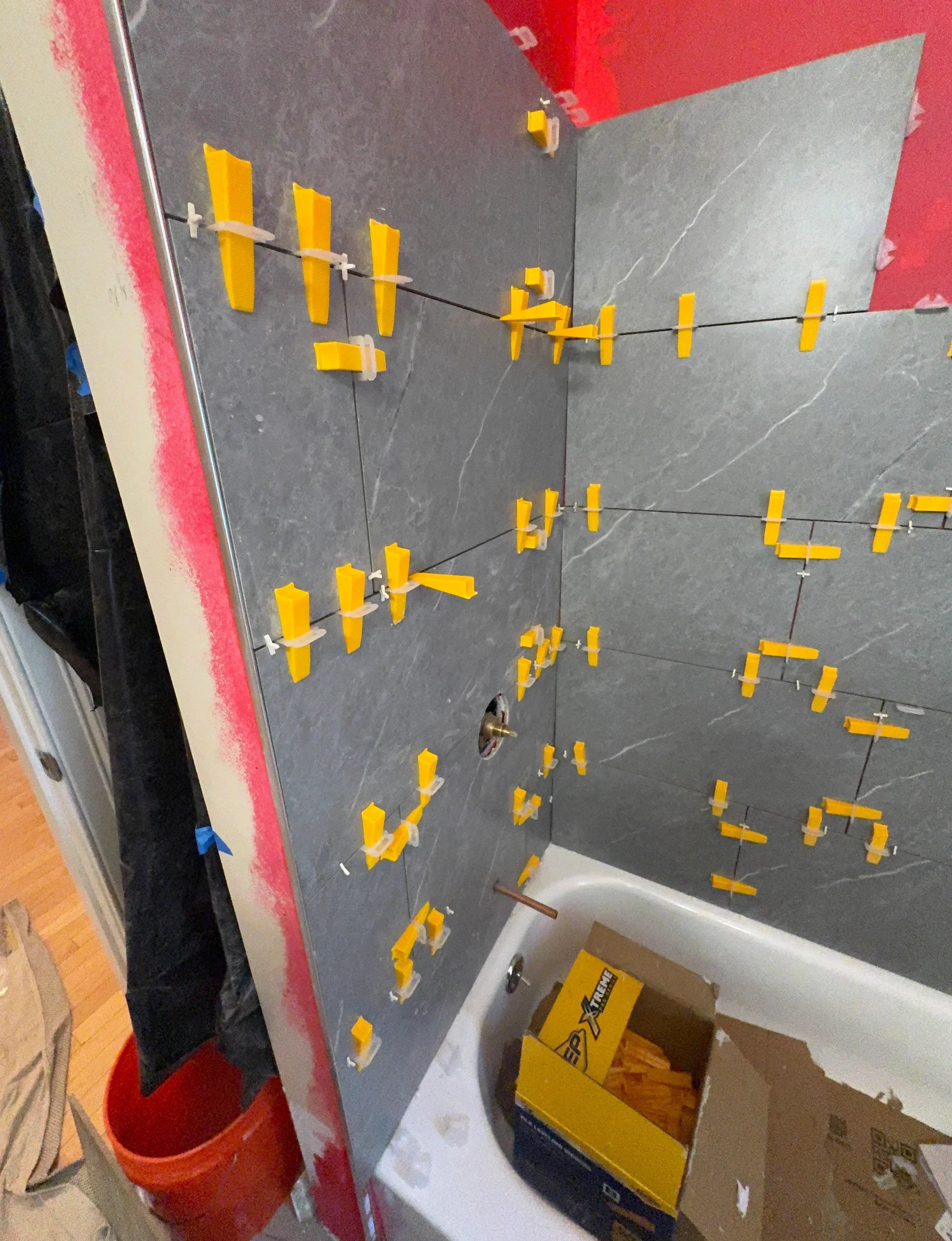 Dark gray tiles with yellow spacers and leveling guides arranged for bathroom shower installation